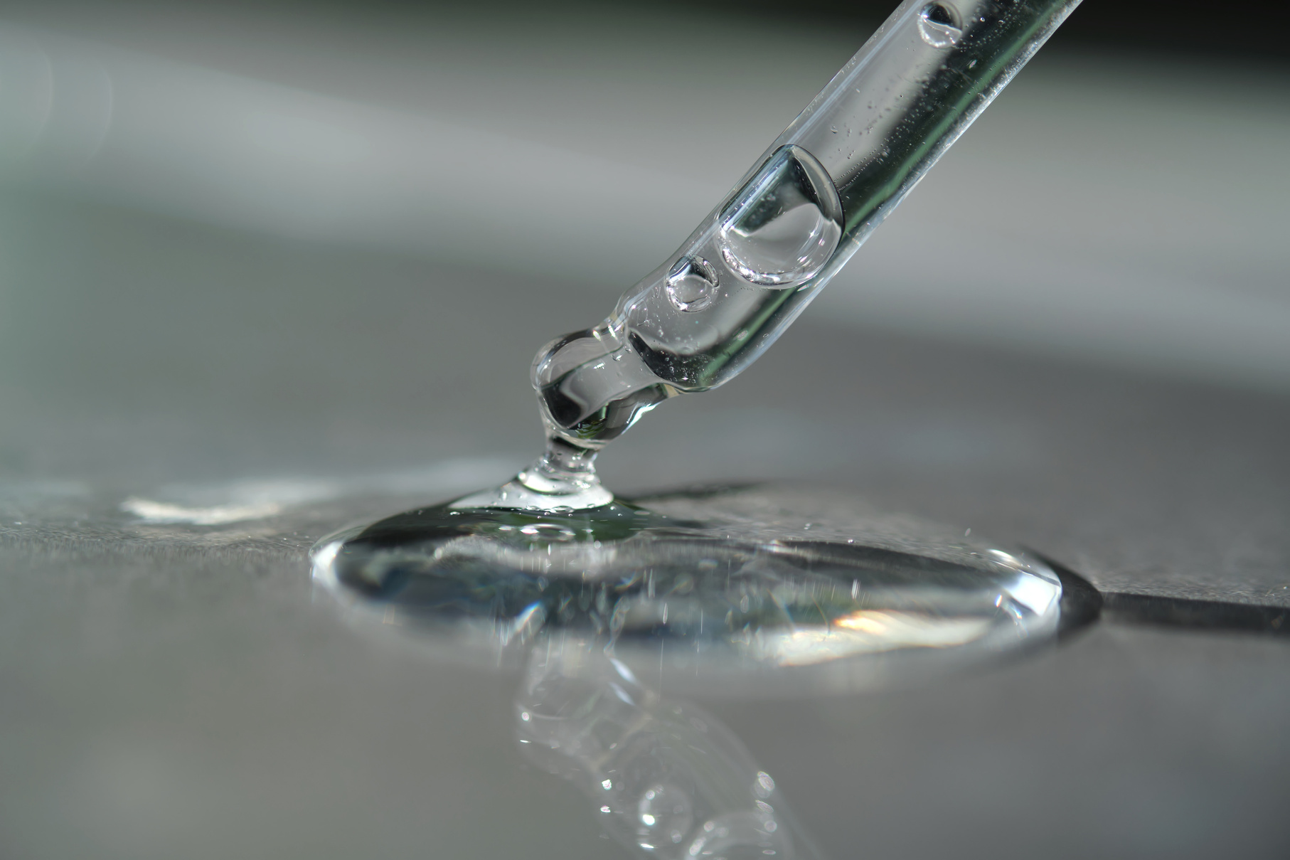 Pipette with spilled cosmetic oil or serum on a gray background.